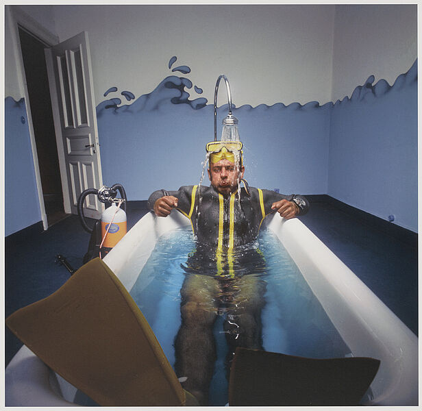 Fotografie eines Mannes, der in einem Taucheranzug in einer Badewanne sitzt