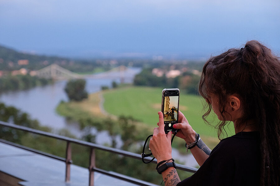 Frau betrachtet Elbhänge durch Smartphone auf den Terassen des Lingnerschlosses