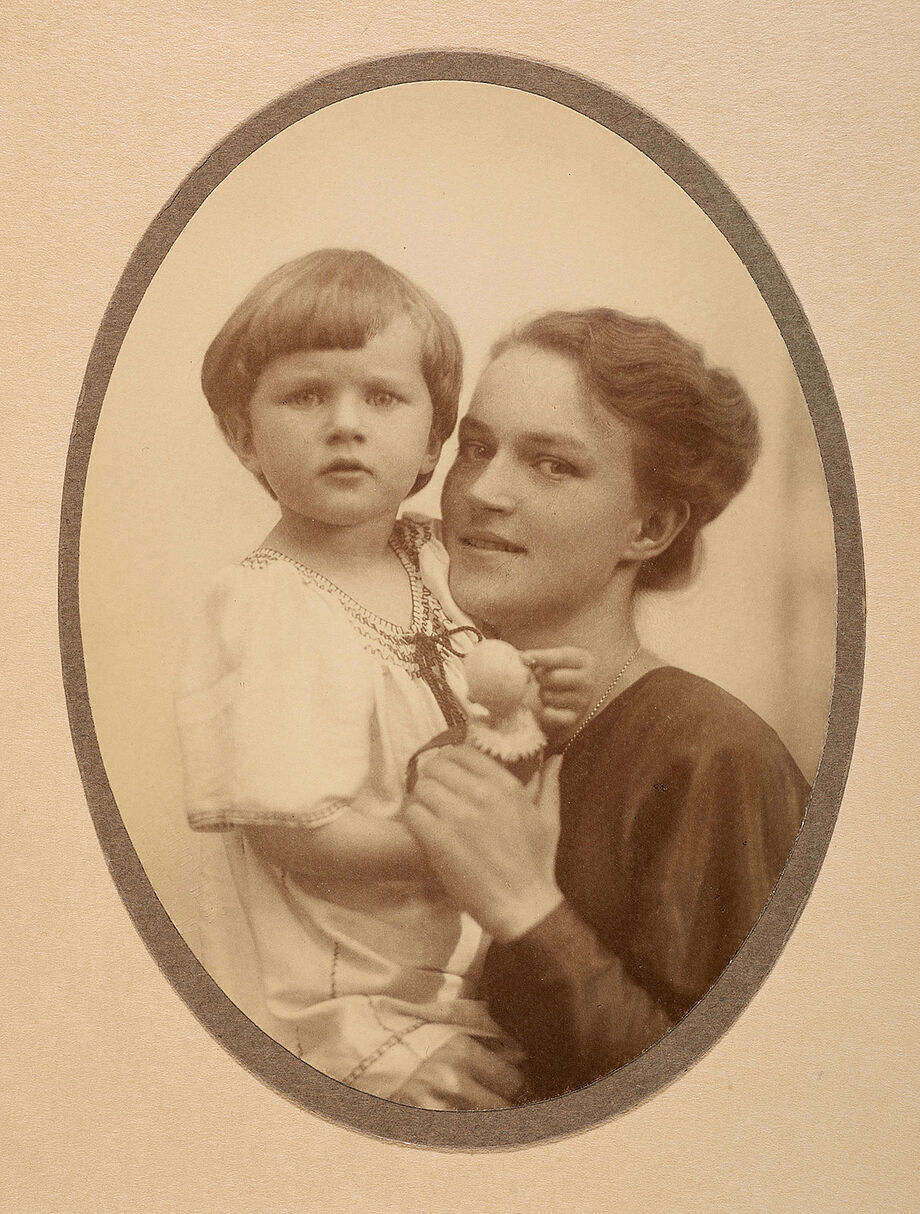 Elise Drescher hält ihre Tochter Renate. Renate trägt ein weißes Kleid und hält eine kleine Puppe in der Hand.